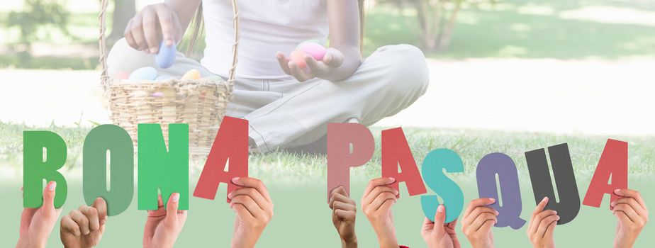 Hands holding up bona pasqua against little girl sitting on grass counting easter eggs smiling at camera