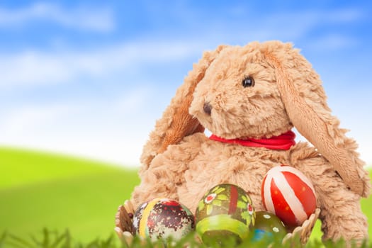 Rabbit, sit on green grass and group of colorful eggs are behind with blue sky background for happy easter festival