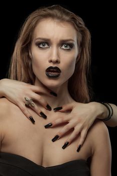 Closeup portrait of a gothic young woman with hands on neck on black background