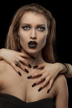 Portrait of a gothic young woman with hands on neck on black background