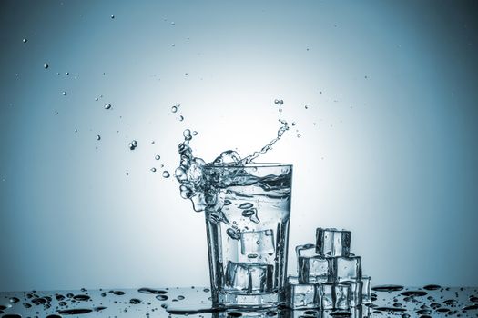 ice cubes falling into a glass of water and ice cubes, lying next, on blue background