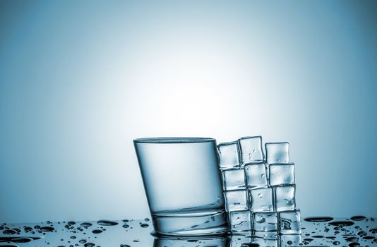 a glass of water and ice cubes, lying next, on blue background