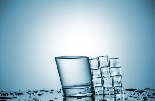 a glass of water and ice cubes, lying next, on blue background