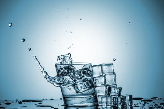 ice cubes falling into a glass of water and ice cubes, lying next, on blue background