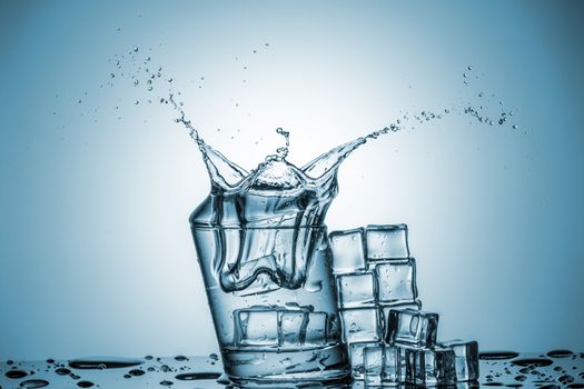 ice cubes falling into a glass of water and ice cubes, lying next, on blue background