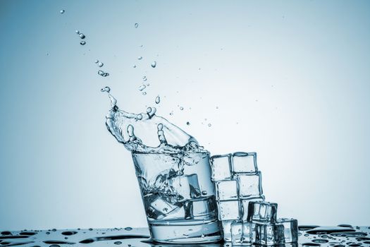 ice cubes falling into a glass of water and ice cubes, lying next, on blue background