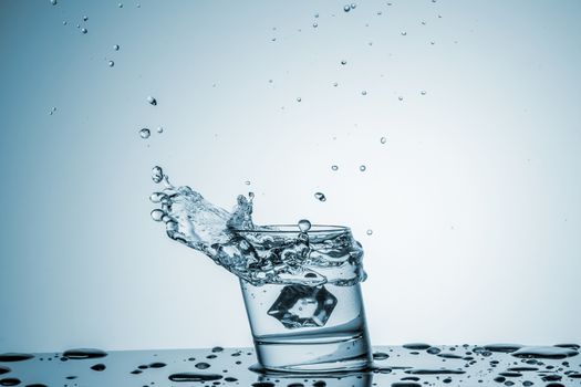 ice cube falling into a glass of water on blue background