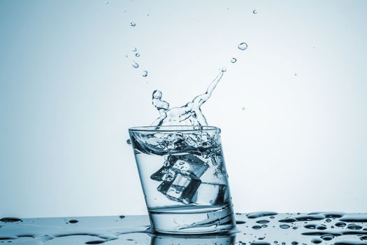 ice cube falling into a glass of water on blue background