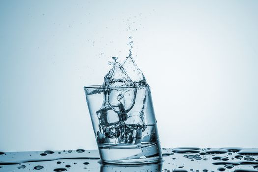 ice cubes falling into a glass of water on blue background