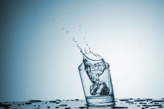 ice cube falling into a glass of water on blue background