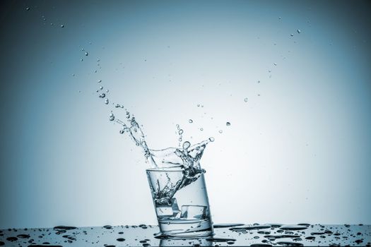 ice cube falling into a glass of water on blue background