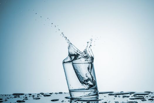 ice cube falling into a glass of water on blue background