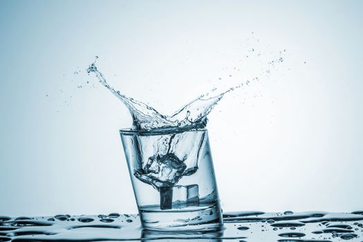 ice cube falling into a glass of water on blue background