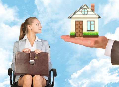 Businesswoman sitting in the chair and looking at house and keys in mans hand