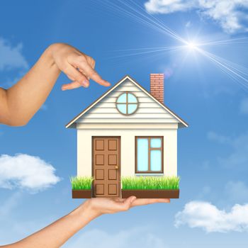Womans hand fingering at house on palm, blue sky background 