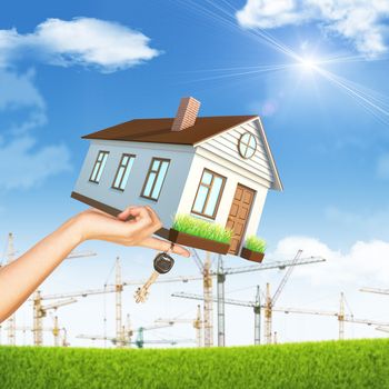 House on businesswomans hand on nature background with building crane