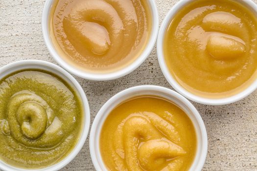 organic fruit and vegetable baby food or snack (apple, pea, spinach, corn, sweet potato, grape, peach) - top view of ceramic bowls