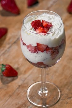 Glass with whipped cream and strawberries into small pieces