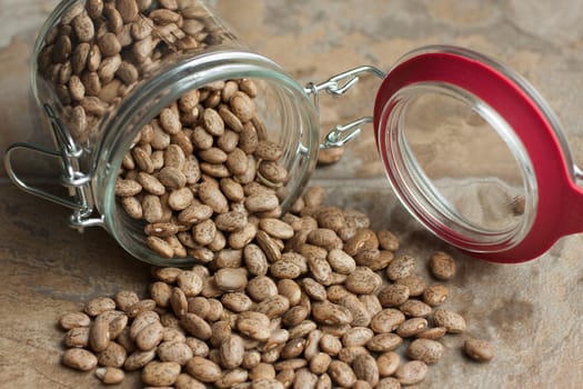 Pinto beans spilling from a glass jar on a tile counter top.