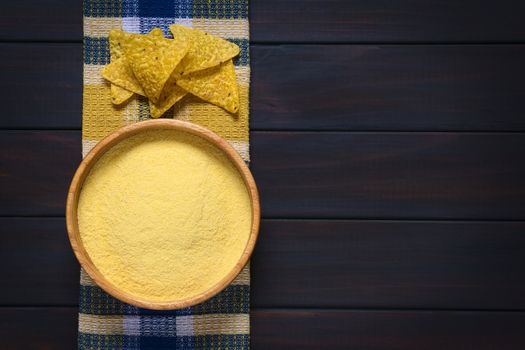 Overhead shot of cornmeal in wooden bowl with tortilla chips on kitchen towel, photographed on dark wood with natural light