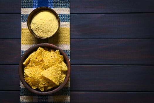 Overhead shot of tortilla chips and cornmeal in bowls on kitchen towel, photographed on dark wood with natural light