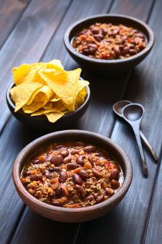 Two rustic bowls of chili con carne with tortilla chips in the back, photographed with natural light (Selective Focus, Focus in the middle of the chili)