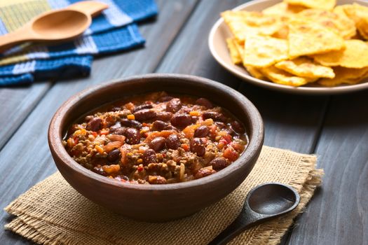 Rustic bowl of chili con carne with homemade tortilla chips in the back, photographed with natural light (Selective Focus, Focus one third into the chili)