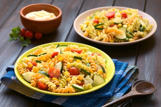 Two plates of vegetarian pasta salad made of tricolor fusilli, sweet corn, cucumber and cherry tomato with mayonnaise in the back, photographed with natural light (Selective Focus, Focus one third into the first salad) 