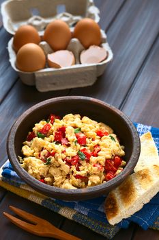 Scrambled eggs made with red bell pepper and green onion in rustic bowl with toasted bread on the side and eggs in the back, photographed with natural light (Selective Focus, Focus one third into the scrambled eggs) 
