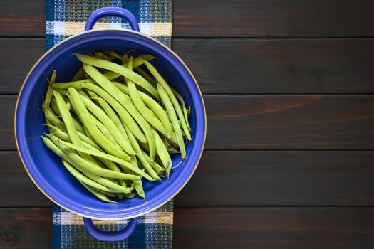 Overhead shot of green beans in blue metal strainer, photographed on dark wood with natural light