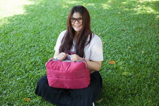 Female student sitting on the lawn. Pink bag was placed on it.