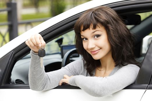 Pretty female driver in a white car showing the car key