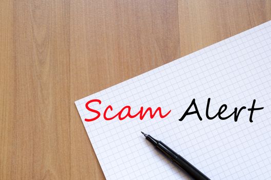 White blank notepad on office wooden table Scam Alert concept