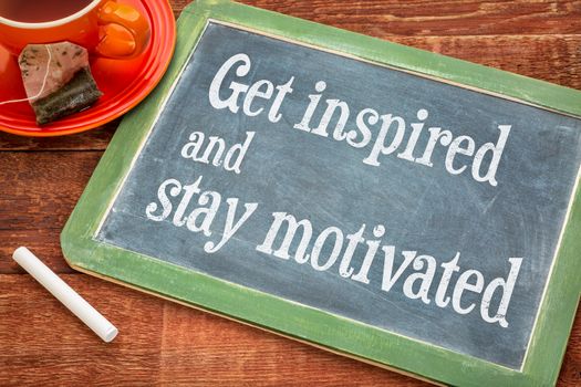 get inspired and stay motivated - motivational teax on a slate blackboard with chalk and cup of tea