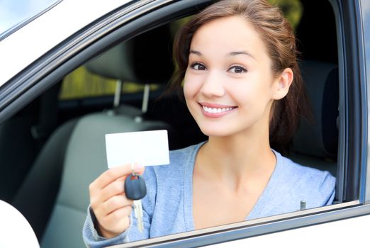Happy girl in a car showing a key and an empty white card for your message