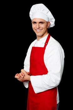 Smiling confident chef posing with hands clasped isolated over black