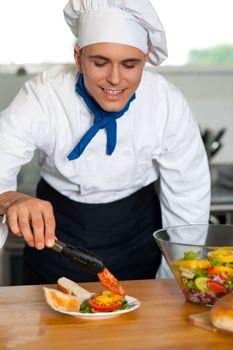Handsome male chef dressed in white uniform decorating salad