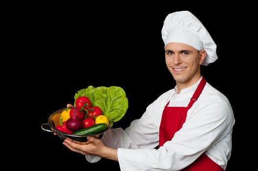 Chef in uniform holding bowl with vegetables isolated on black background