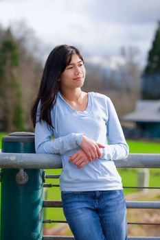 Young biracial teen girl standing, leaning against railing at park