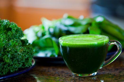 Glass cup of green vegetable juice on kitchen counter, made with kale, spinach.