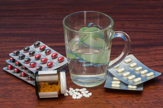 Various pills and water glass are on table