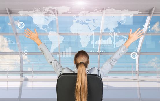 Rear view of businesswoman sitting in chair with arms up in front of window with virtual world map