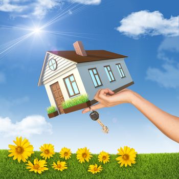 House and keys in left womans hand on nature background with flowers