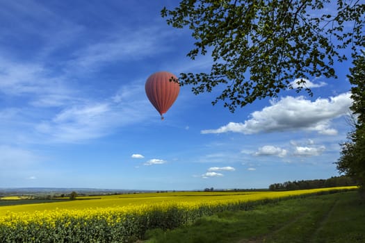 Hot air balloon drifting over field of oilseed rape in the Harwardian Hills in North Yorkshire in the northeast of England.