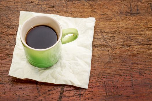 green stoneware cup of espresso coffee on a napkin against rustic wood with a copy space