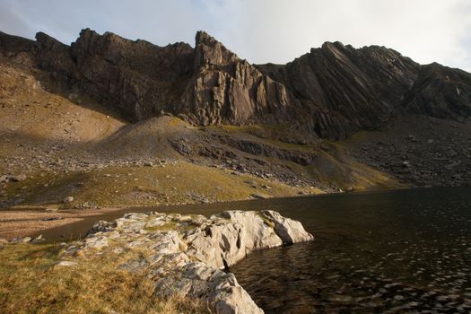 A rocky foreground leads to a lake and the impressive mountain crags of Clogwyn Du'r Arddu, Snowdonia national park, Wales, UK.