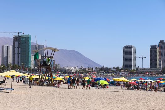 IQUIQUE, CHILE - JANUARY 23, 2015: Lifeguard watchtower, sunshades and many visitors on Cavancha beach on January 23, 2015 in Iquique, Chile. Iquique is a free port city in Northern Chile.