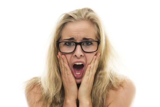 Attractive young woman with long blond hair wearing glasses reacting with a horrified anxious expression holding her hands to her cheeks with her mouth wide open, on white