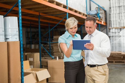 Warehouse managers looking at tablet pc in a large warehouse