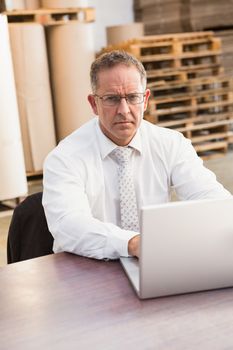 Serious warehouse manager using laptop in a large warehouse